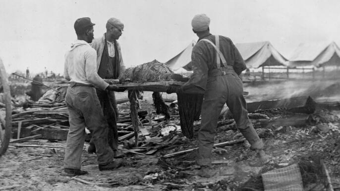 Men carrying a body on a stretcher, surrounded by wreckage of the hurricane and flood in Galveston, Texas, 1900. (Credit: Buyenlarge/Getty Images)