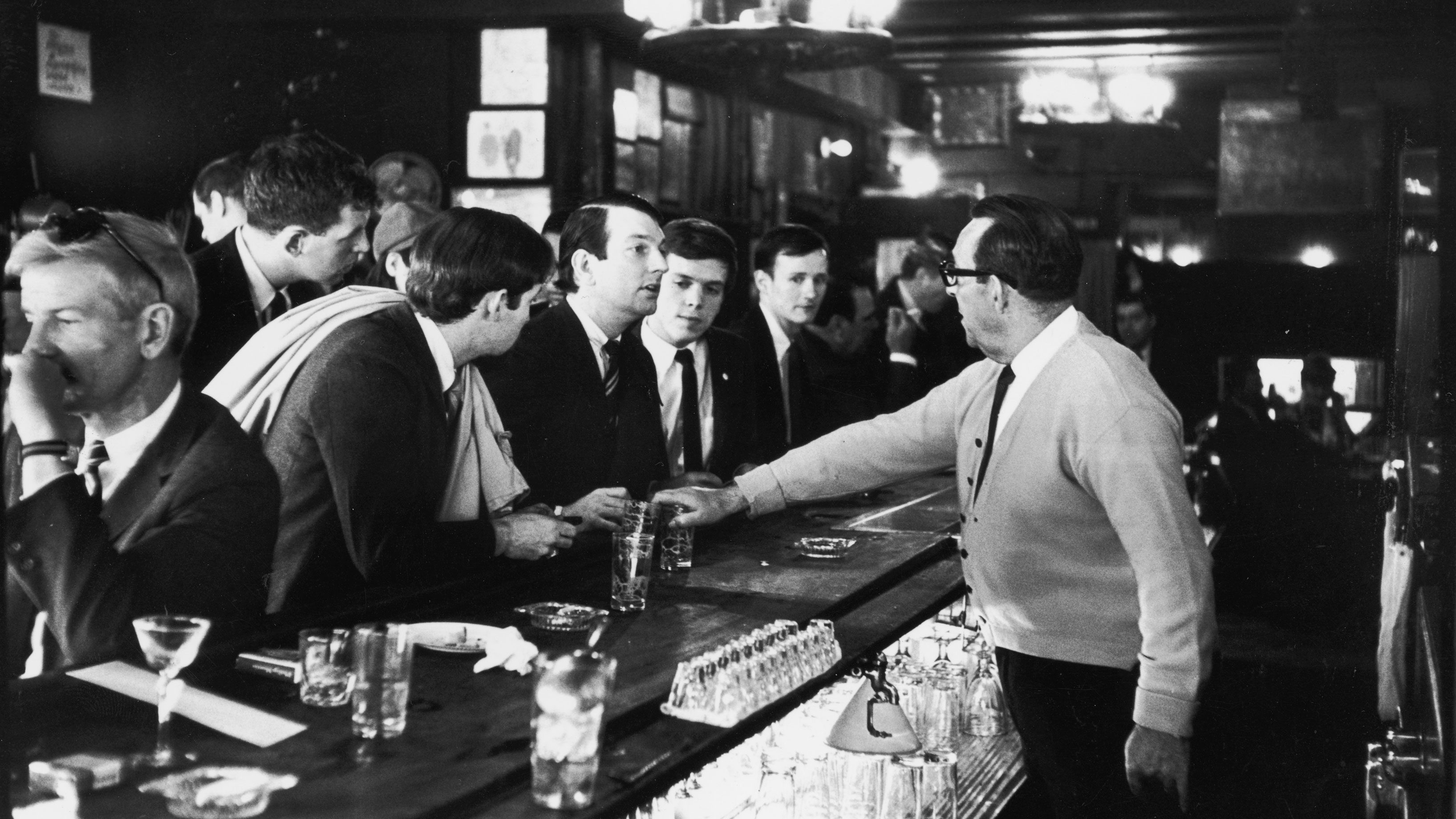 bartender takes drink of men sitting at bar