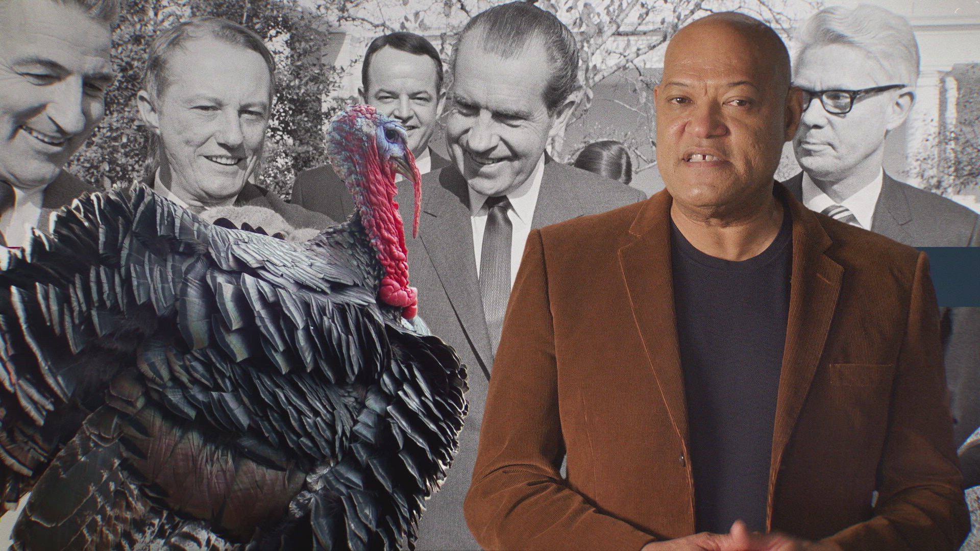 host laurence fishburne stands in front of a backdrop photo of richard nixon pardoning a turkey