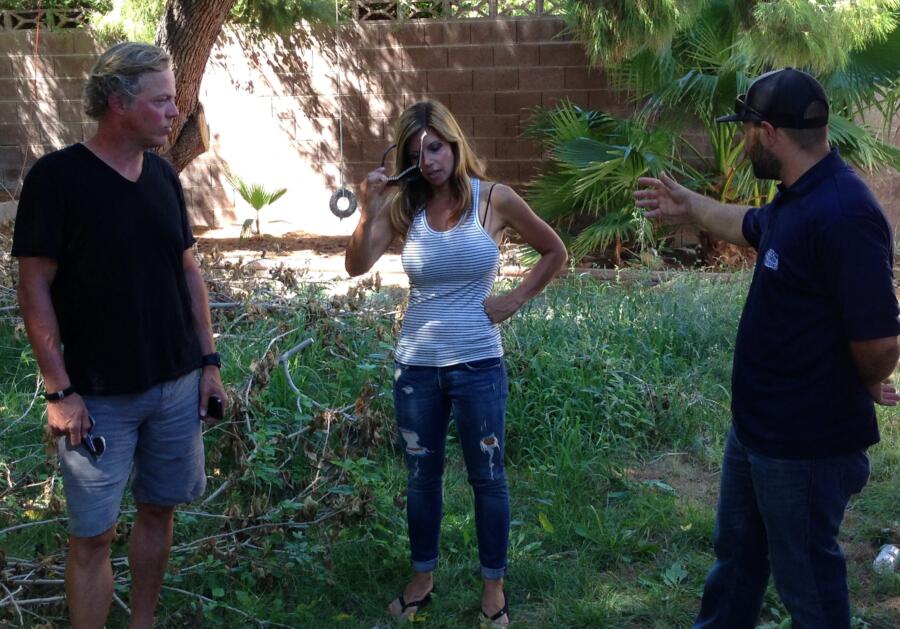 Scott and Amie stand in a disheveled backyard with their landscaping contractor to discuss possible landscape options.