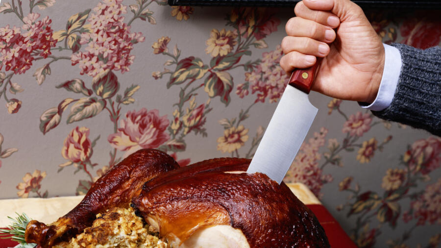 Man's hand cutting cooked turkey with knife