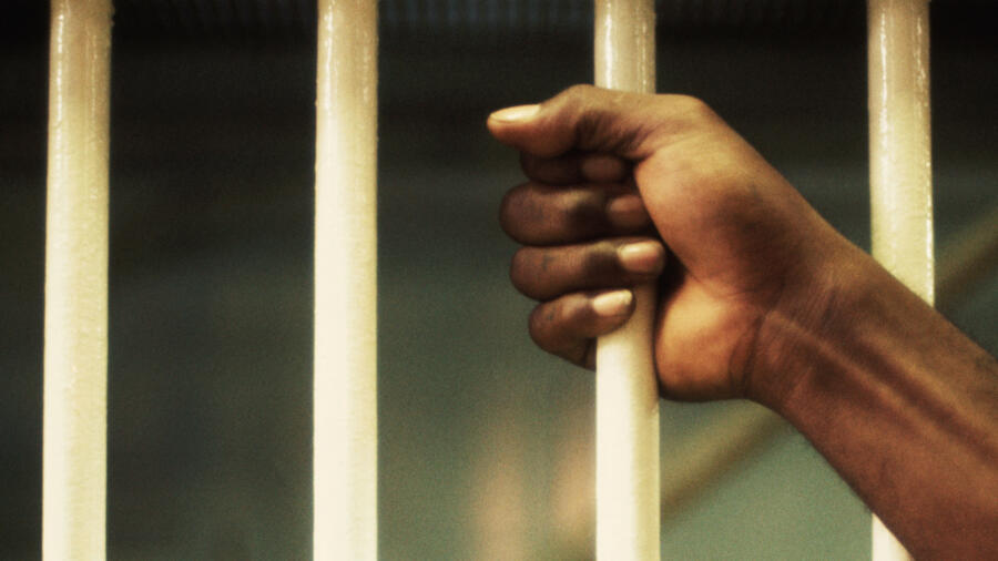 A prisoner holds onto a prison cell bar